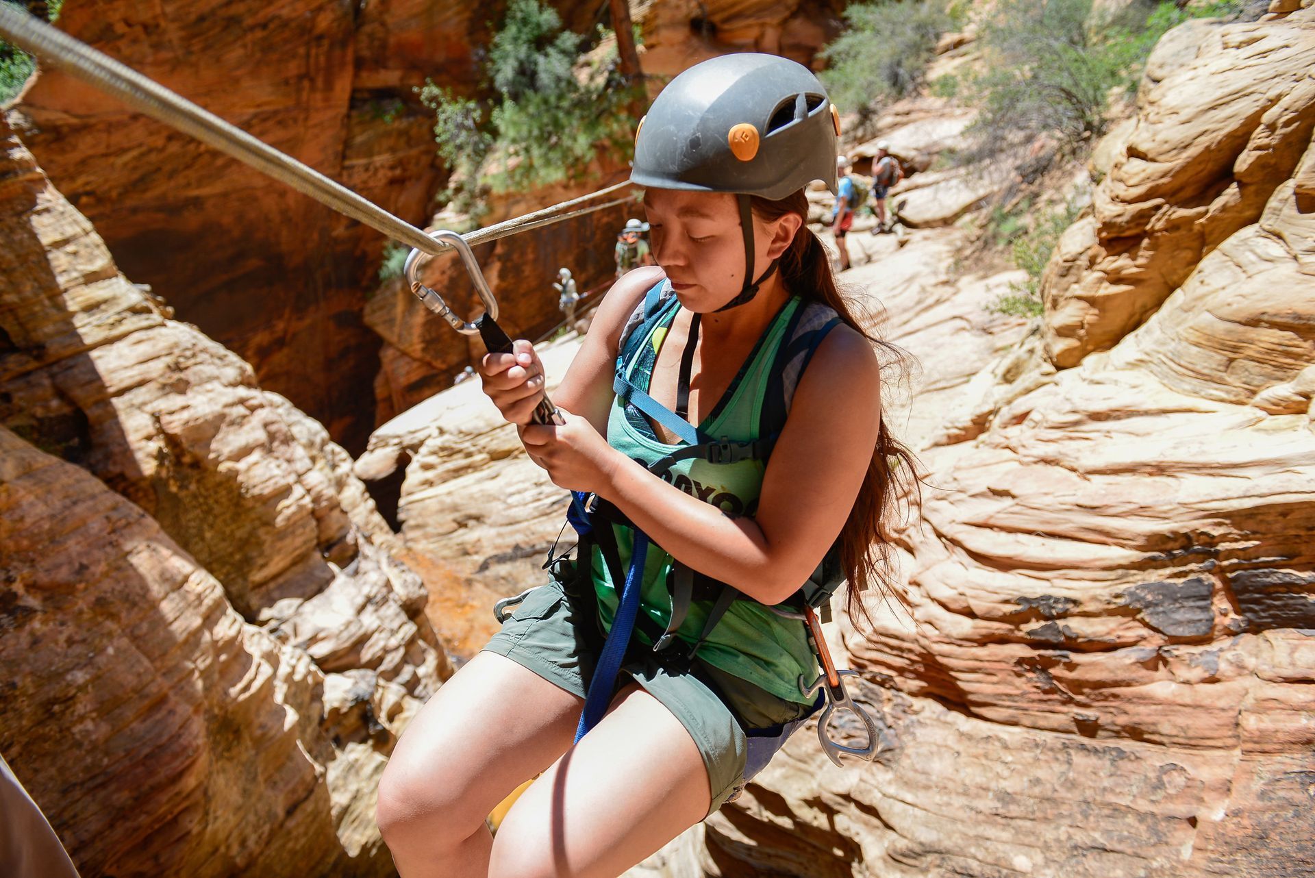 Woman rappelling down a canyon using a rope, wearing a helmet and harness.