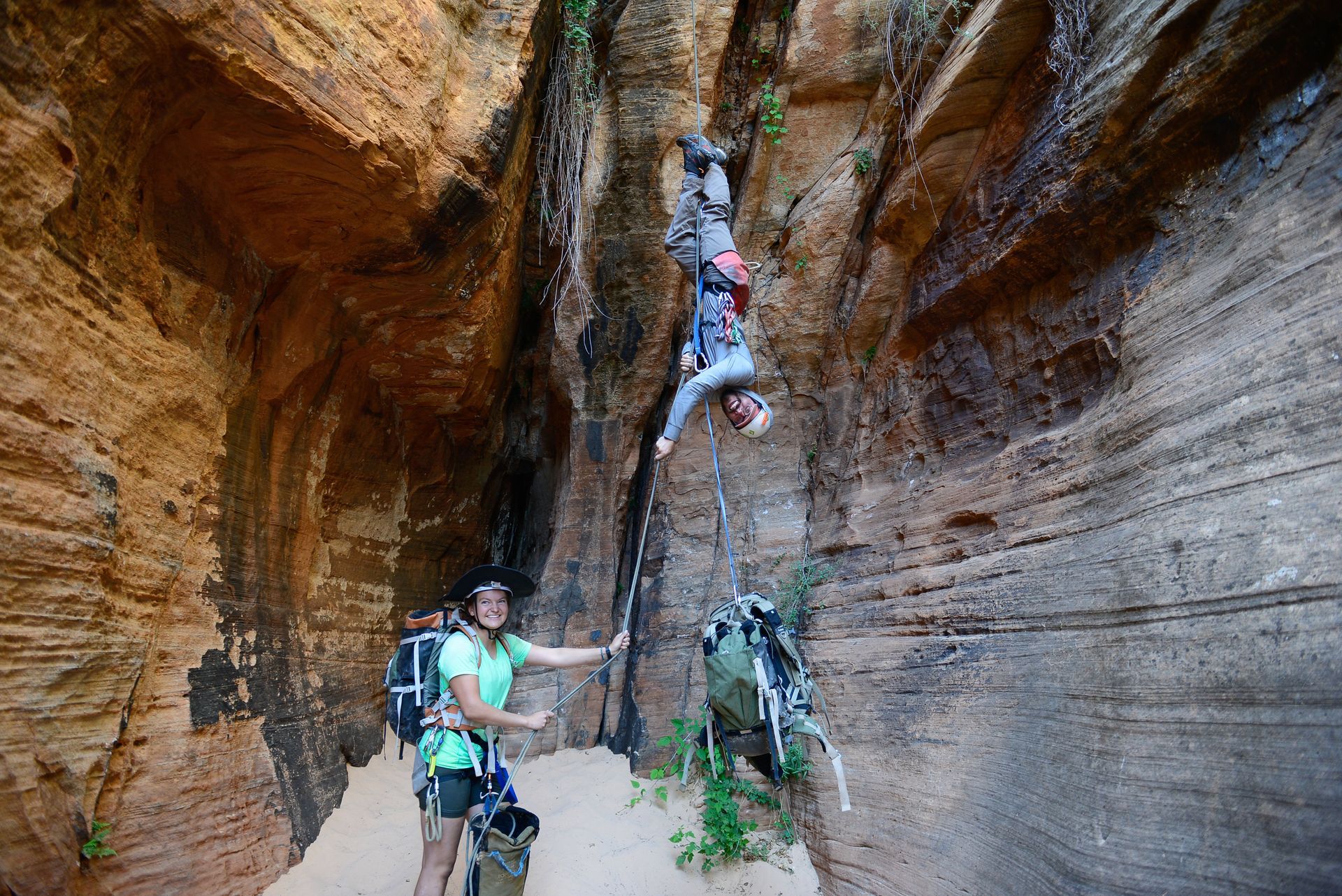 People canyoning; one upside down, others watch. Narrow canyon walls.
