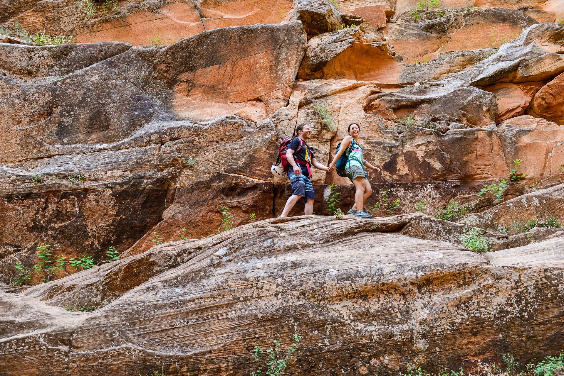 Two people hiking on reddish-brown rock formations.