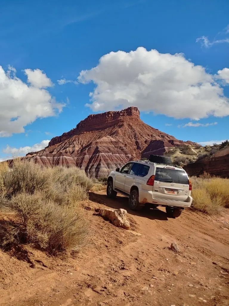 A white suv is parked on a dirt road in front of a mountain.