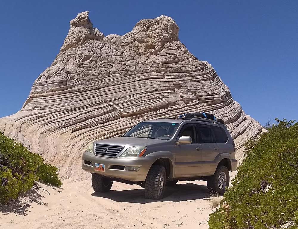 A jeep with a roof rack is driving down a dirt road