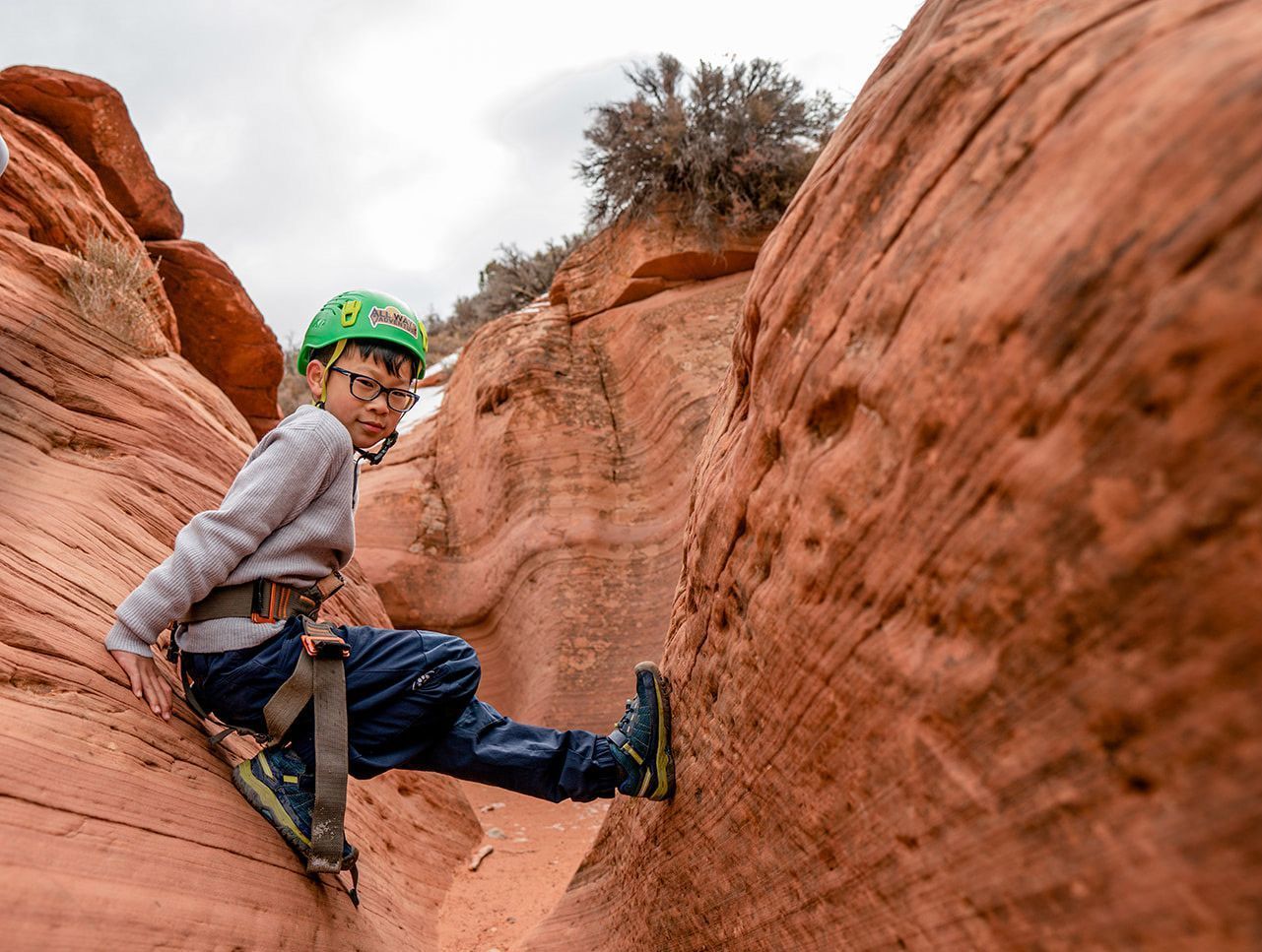 A child with a green helmet balances between red rocks