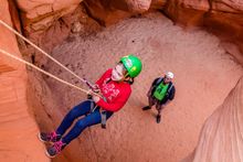 Girl rappelling down a sandstone canyon; instructor watches from above.