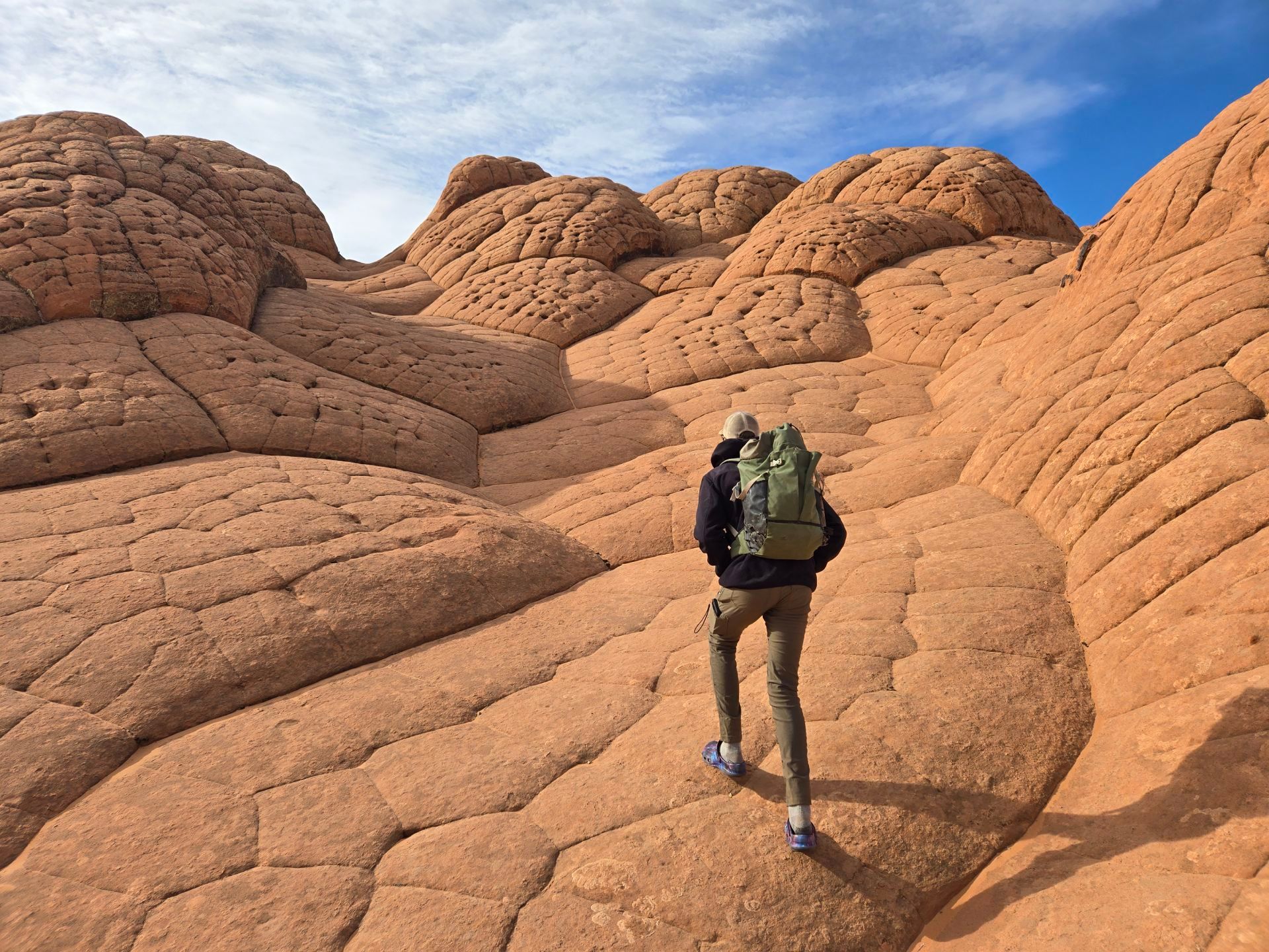 A person hikes an orange sand stone formation in White Pocket