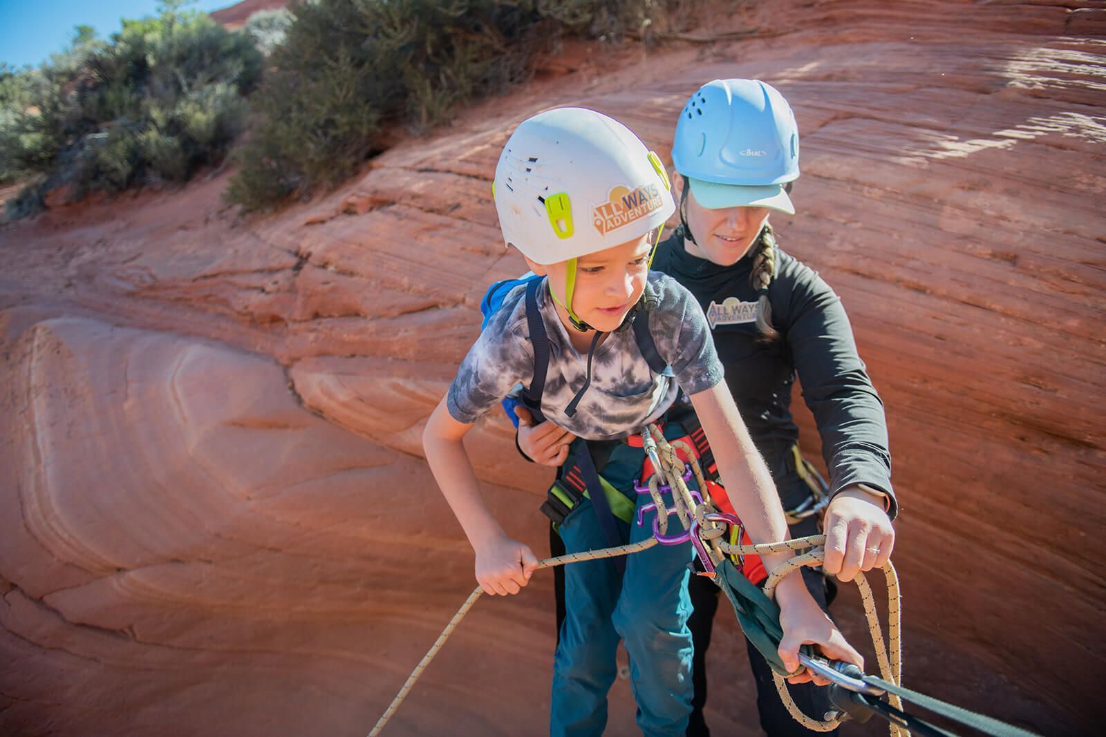 A boy wearing a helmet is helping another boy tie a rope