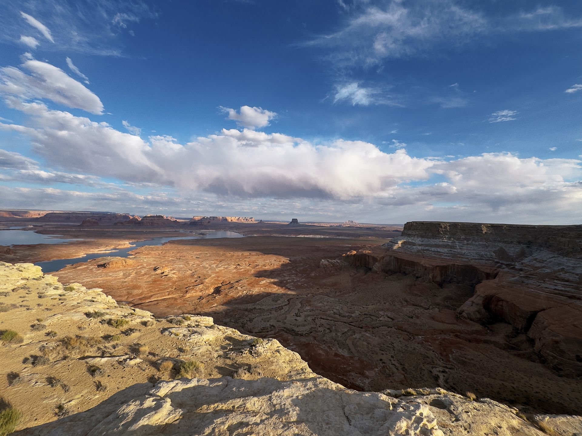 A desert landscape with a lake in the background and a blue sky with clouds