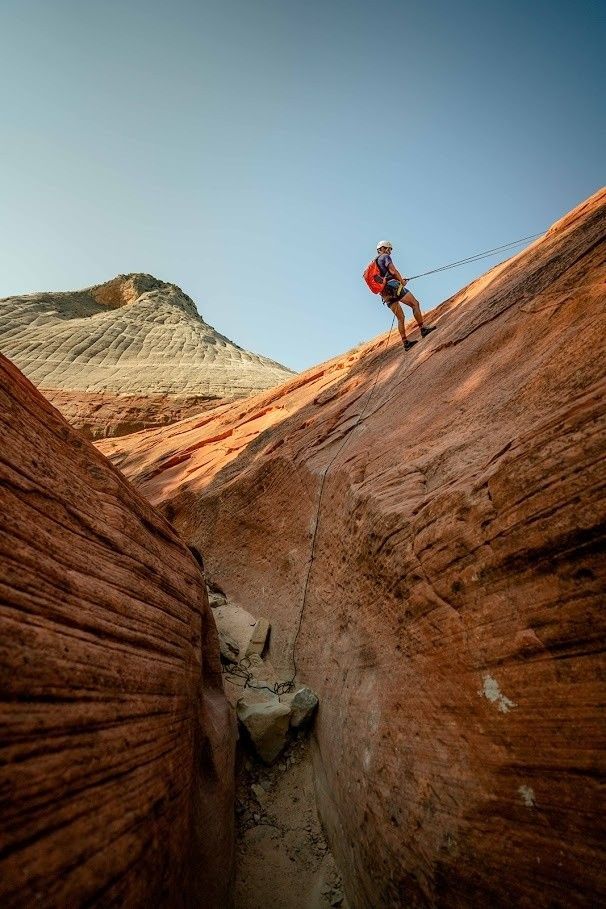 A person is climbing up a rocky cliff with a rope.