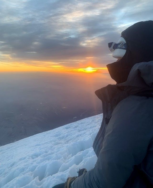 A person looks out at the setting sun from a summit