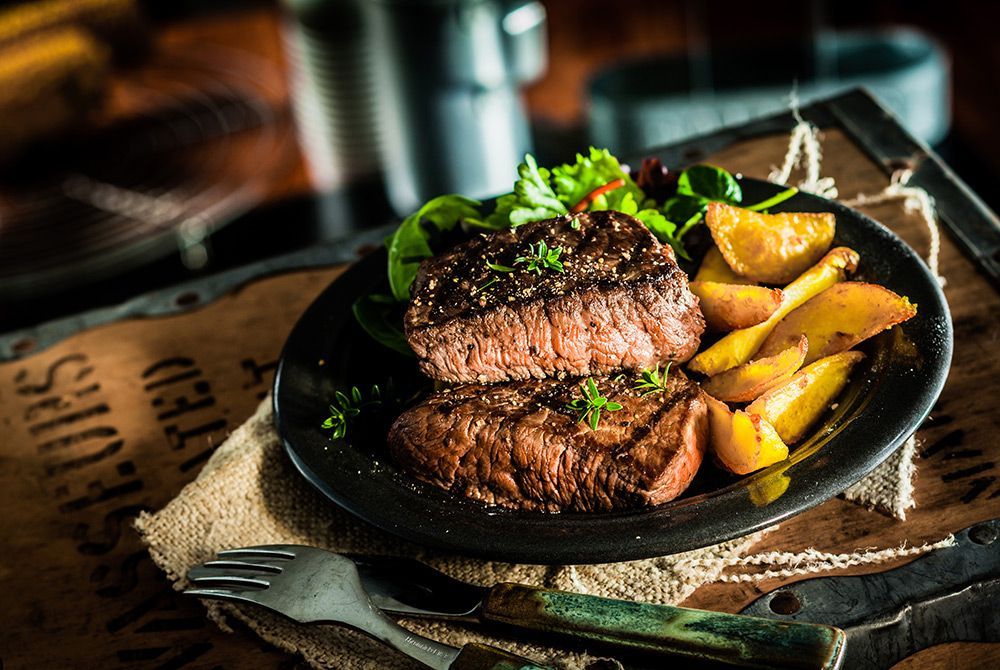 A steak and potatoes on a black plate with a fork