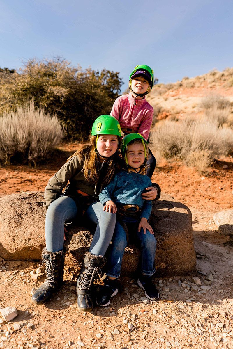 Three children wearing green helmets are sitting on a rock