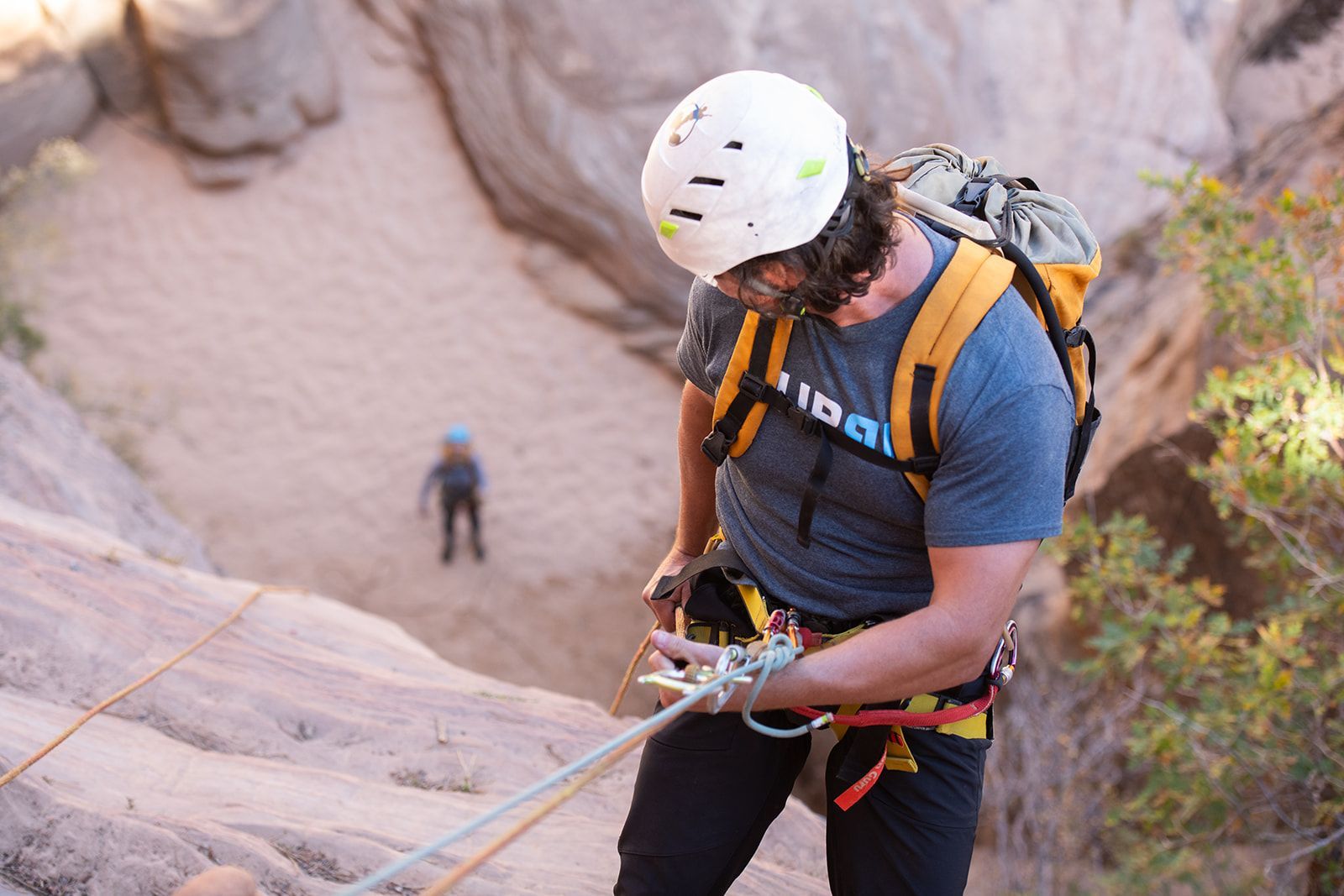 Man in a helmet preparing to rappel down a rock face. Another person in the background.