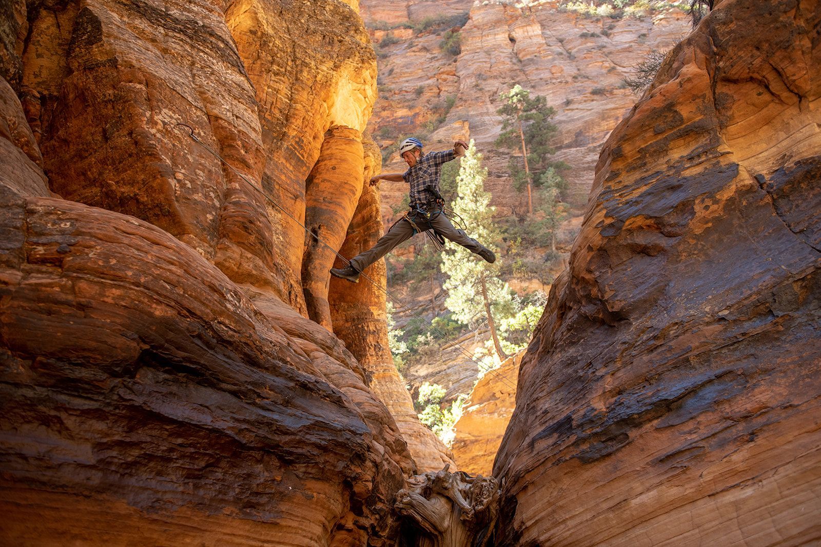 Person jumps across a narrow canyon. Red rock walls surround them.