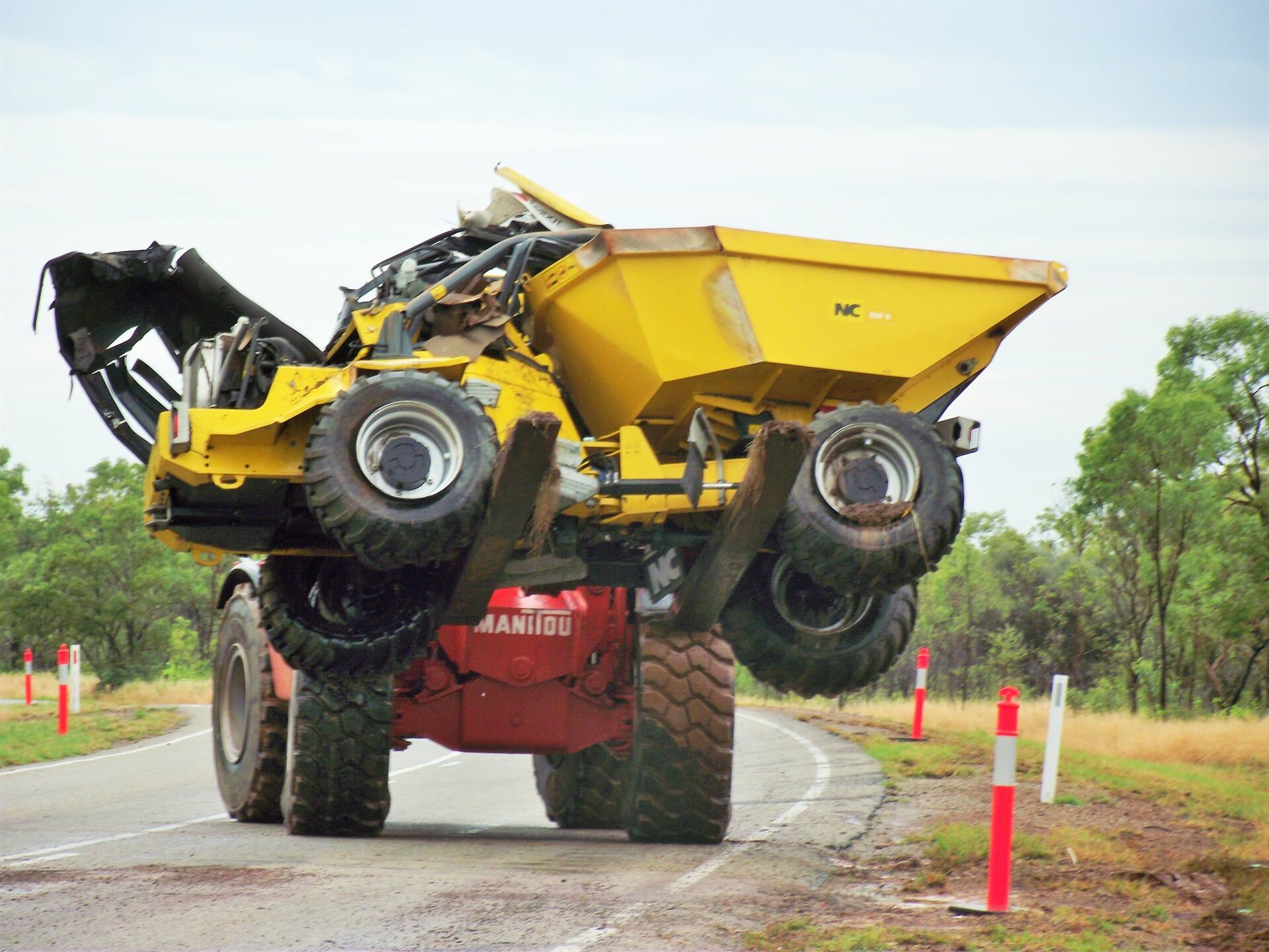 A yellow dump truck with the hood up is driving down a road- Slingshot Haulage in Katherine, NT