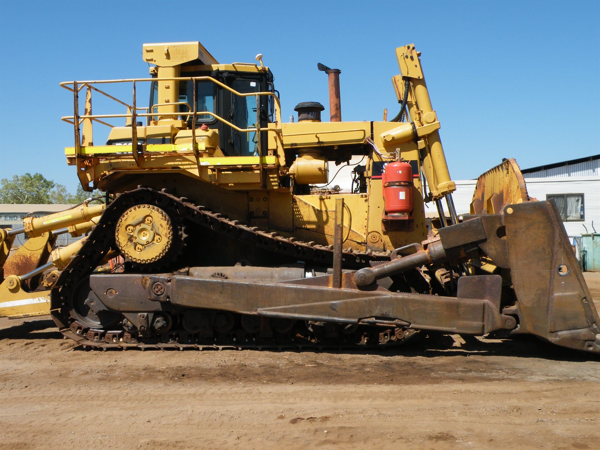 A large yellow bulldozer is parked in a dirt field- Slingshot Haulage in Katherine, NT