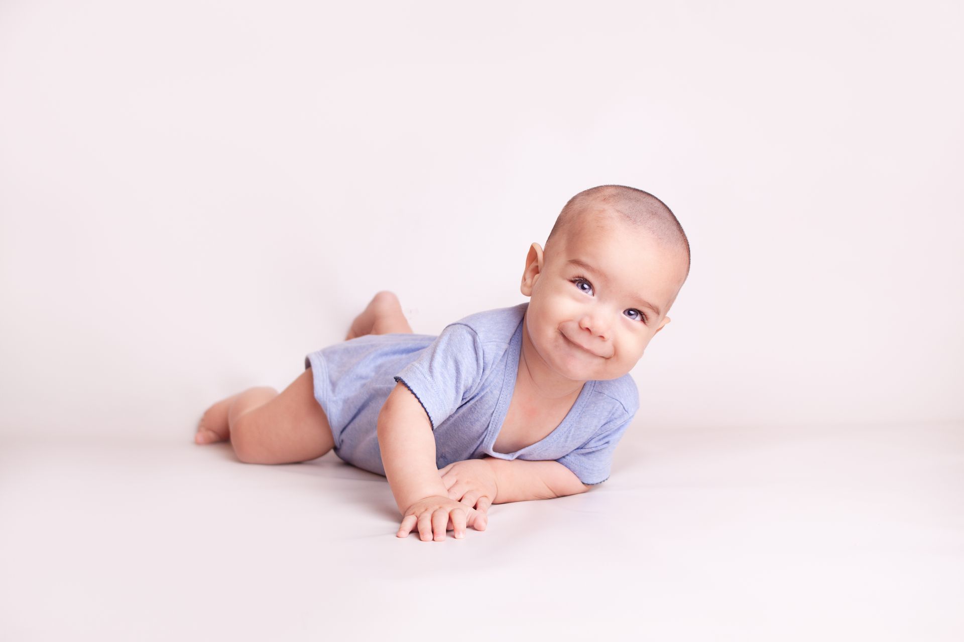 Un bebé gatea boca abajo sobre una superficie blanca y sonríe.