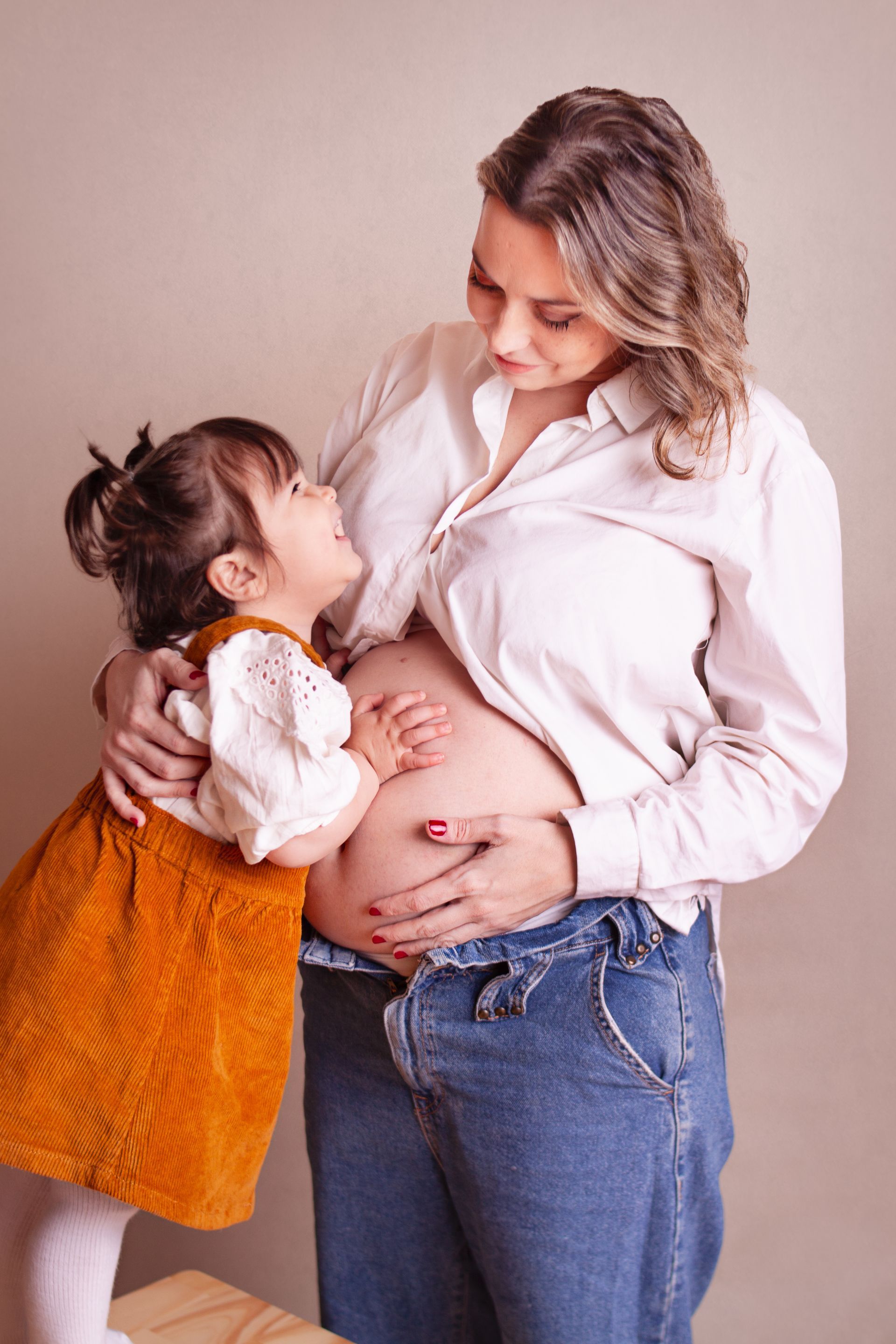 Una niña abraza el vientre de una mujer embarazada.