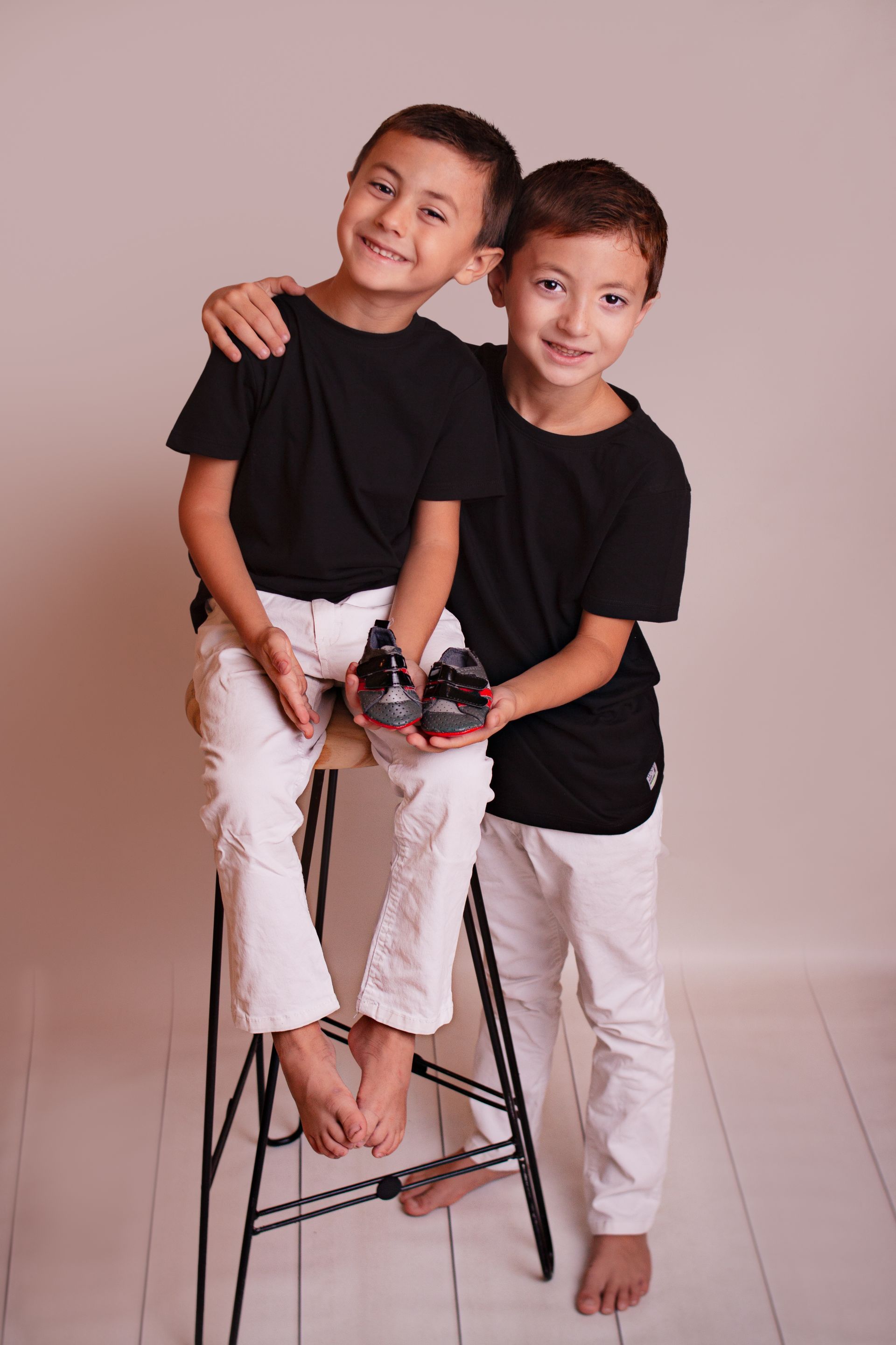Dos niños pequeños están sentados en un taburete sosteniendo un par de zapatos.