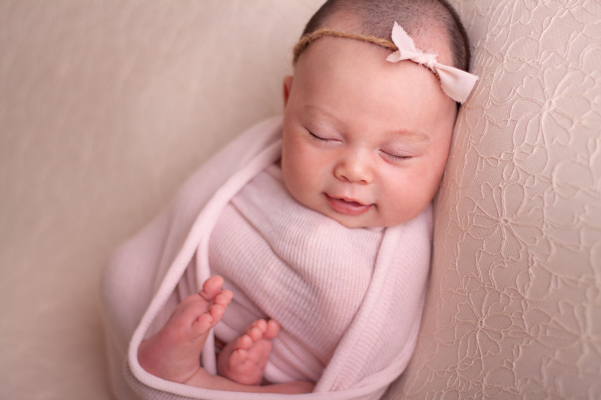 Un bebé recién nacido está envuelto en una manta rosa y lleva una diadema.