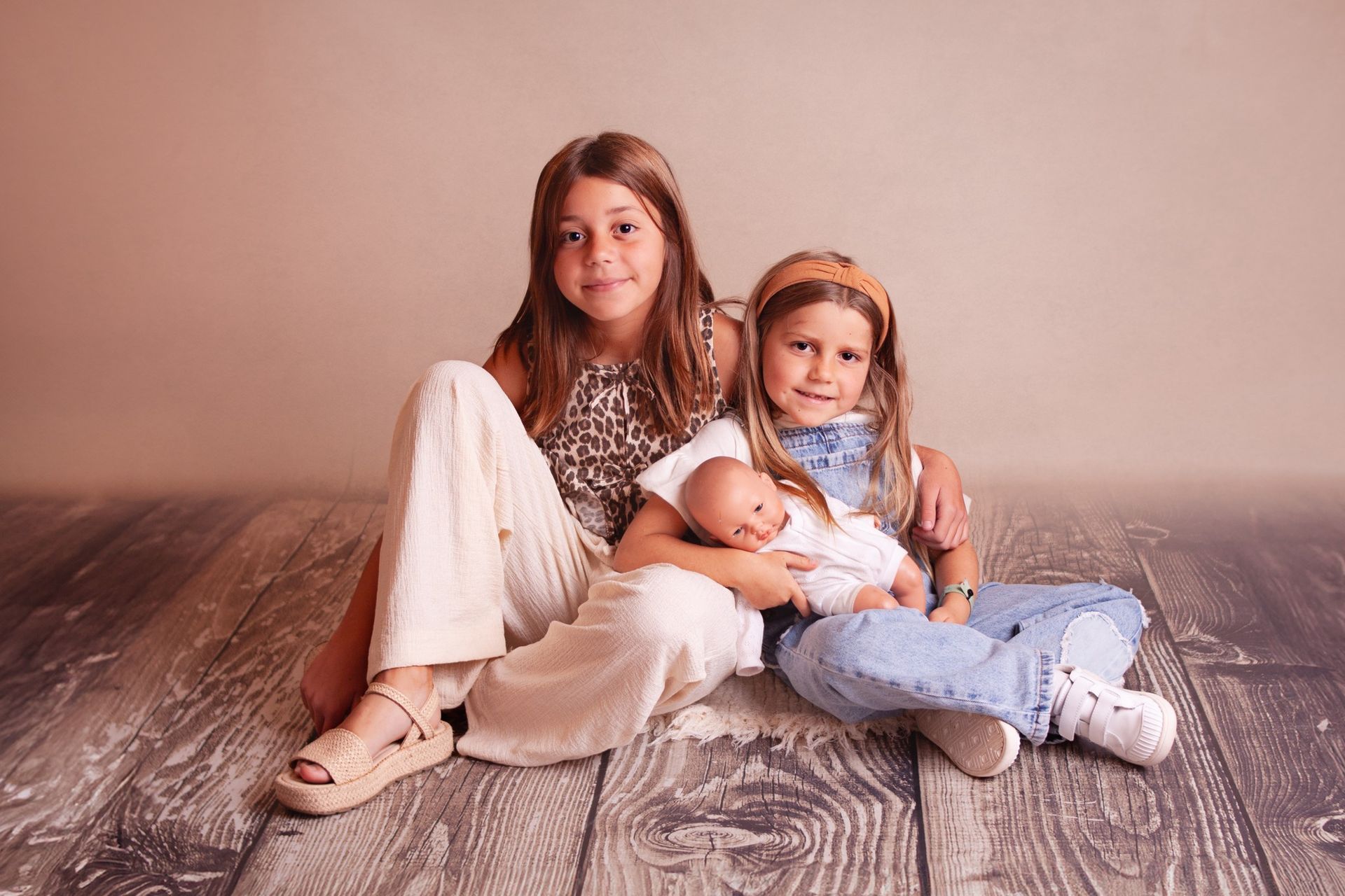 Tres niñas están sentadas en un suelo de madera sosteniendo un bebé.