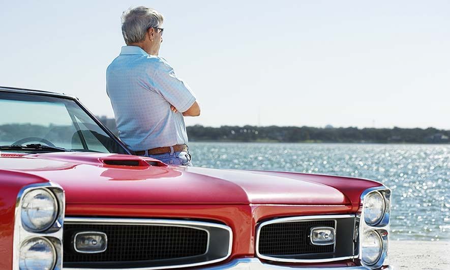 a man leans against his classic car with collectors insurance protection