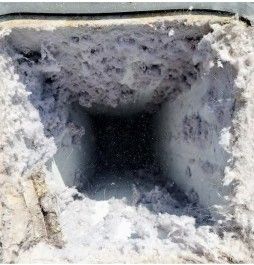 A square hole in a dusty, light-colored surface; the hole appears dark inside.