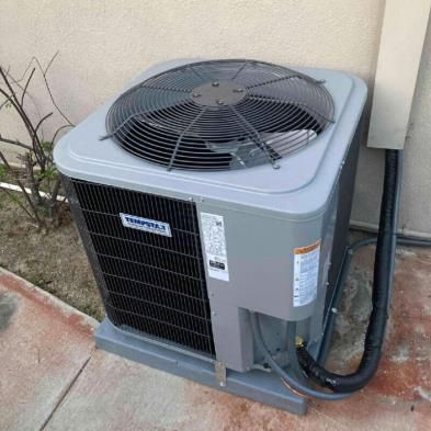 An air conditioner is sitting on the sidewalk outside of a building.