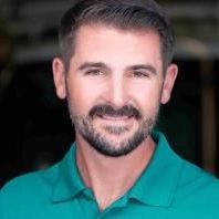 A man with a beard is wearing a green polo shirt and smiling.