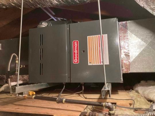 A goodman air conditioner is sitting in the attic of a house.