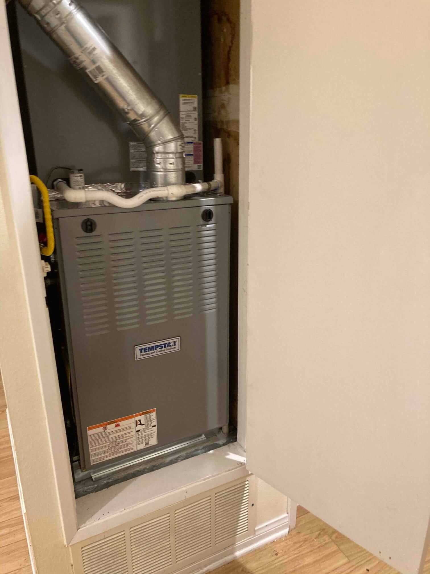 A furnace is sitting inside of a cabinet in a room.