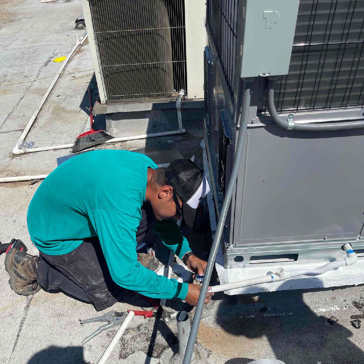 A man is working on an air conditioner on the roof of a building.
