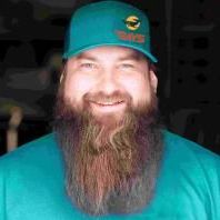 A man with a beard is wearing a hat and smiling.