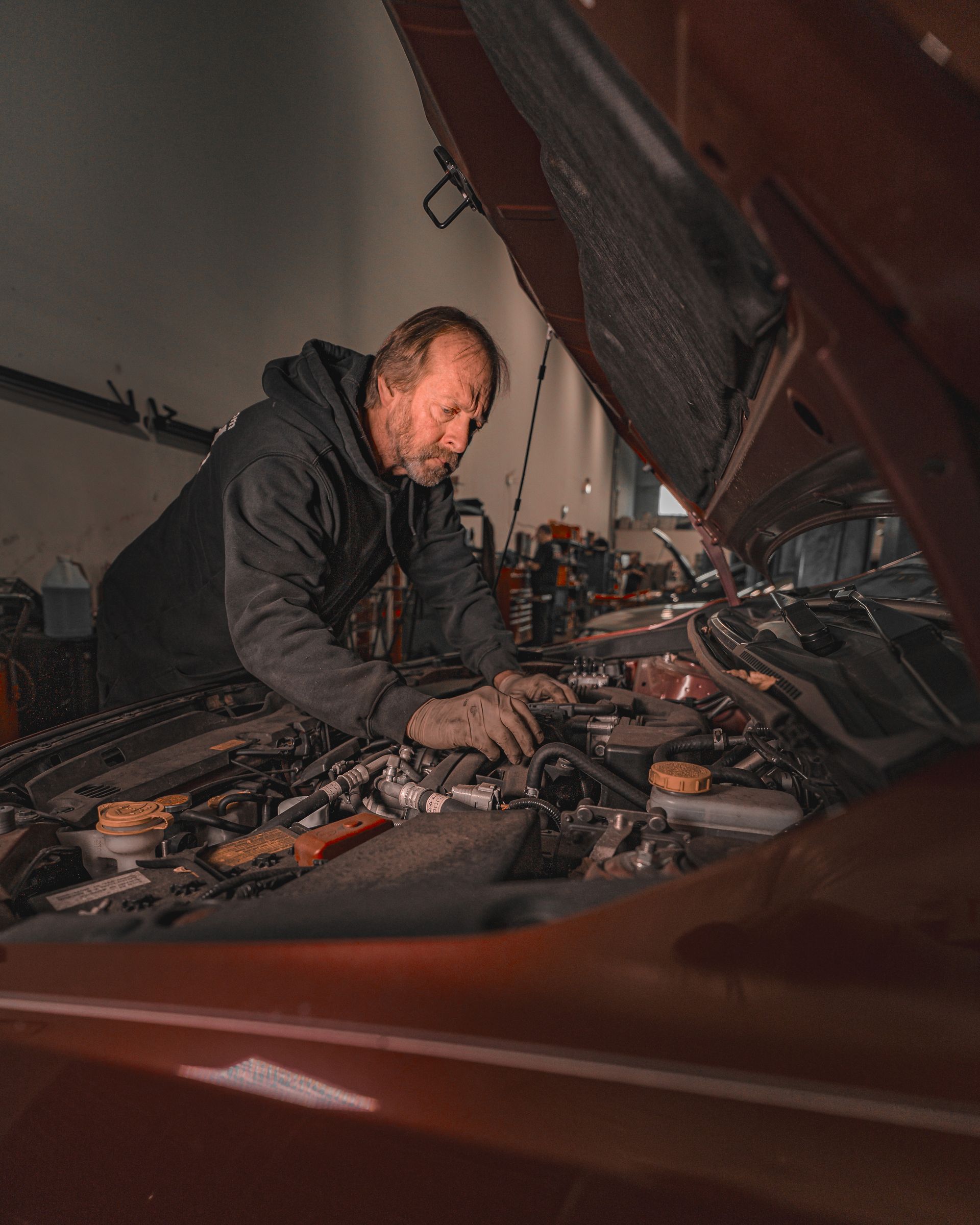 A mechanic dives into the open hood of a car at an auto repair shop.