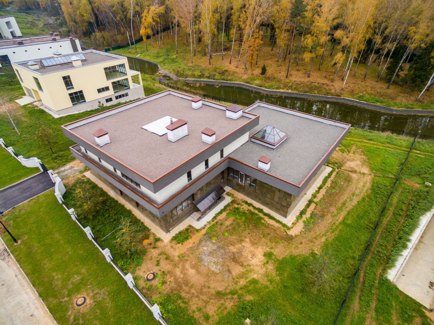 Aerial view of a modern flat-roofed building beside a grassy field and trees
