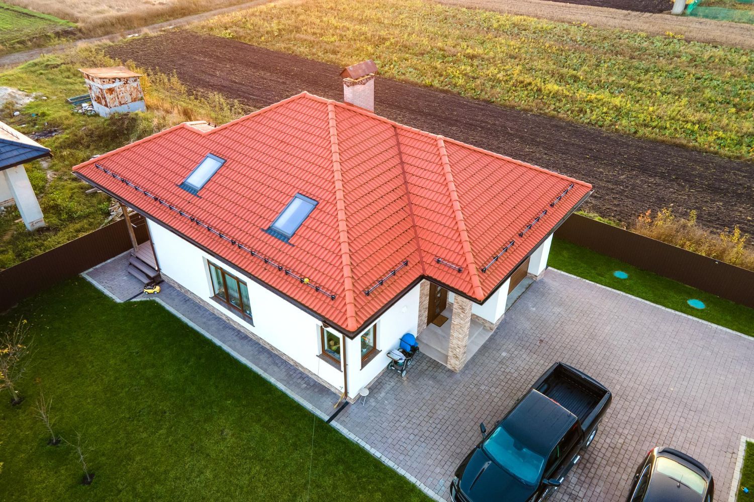 Aerial view of a white house with a red roof beside fields and a driveway with a black car.
