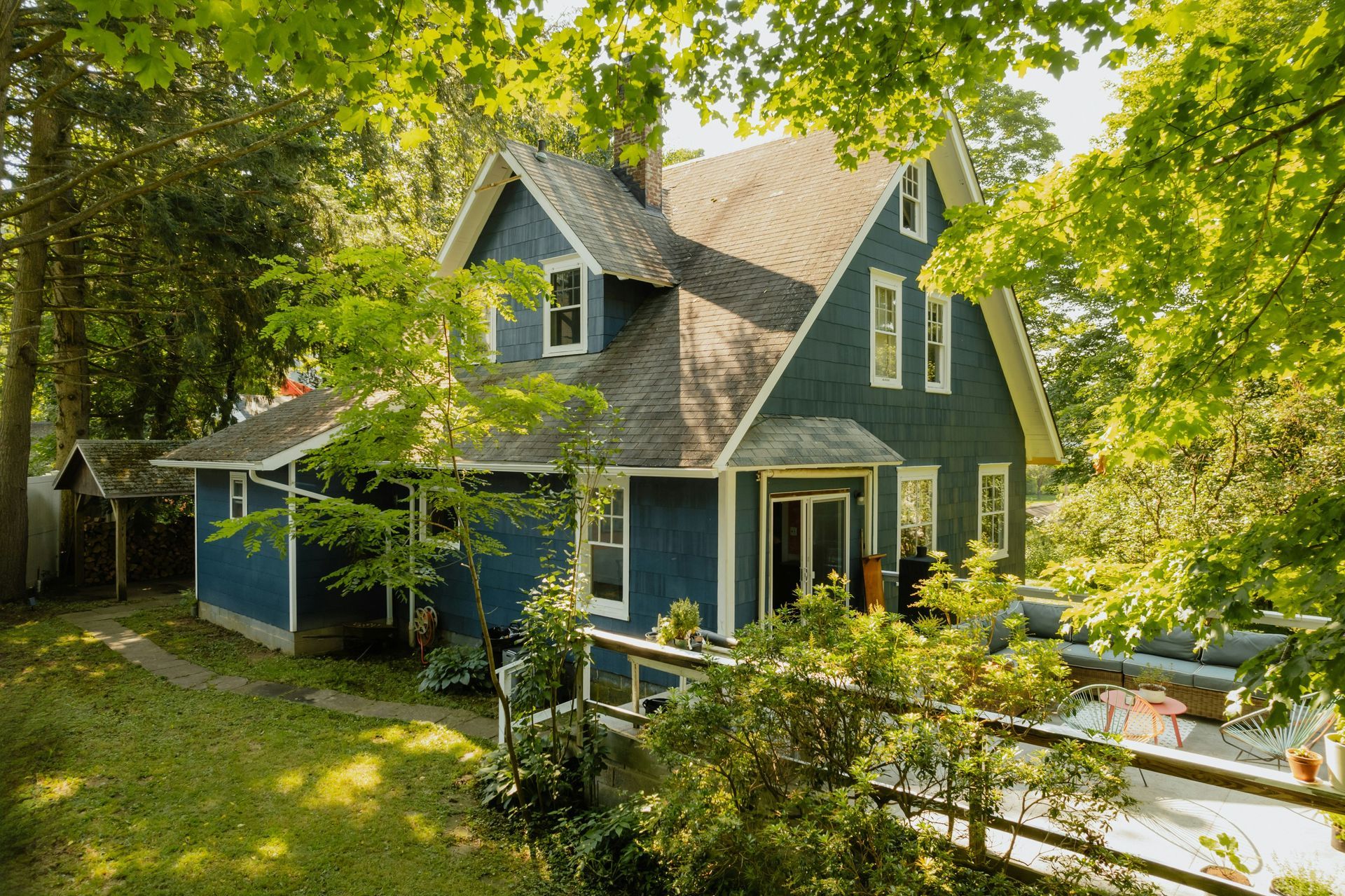 Blue house with white trim in a leafy yard, viewed through sunlit trees