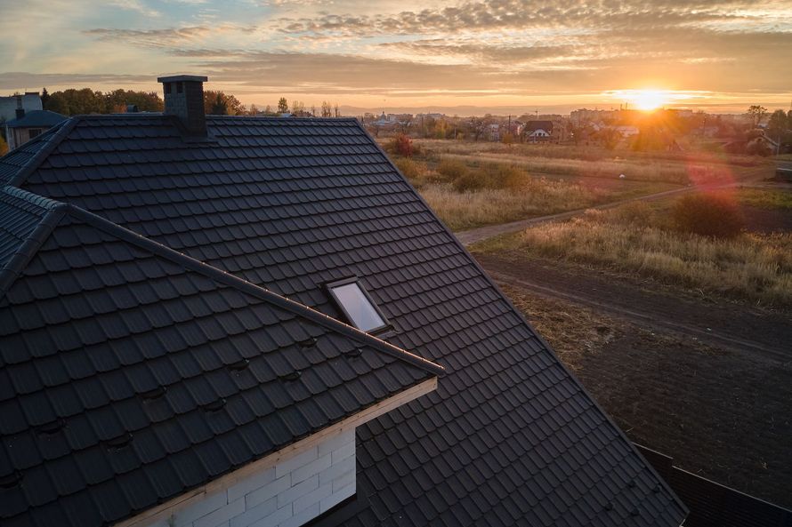 Sunset over a dark tiled roof beside open fields and a winding road