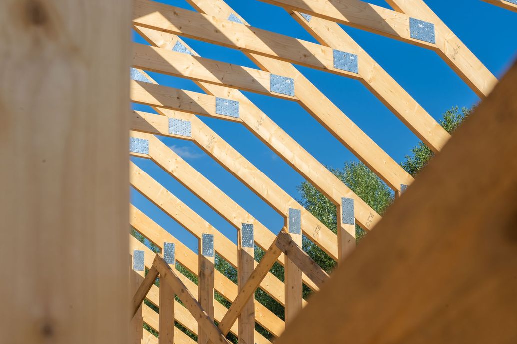 Diagonally arranged wooden beams against a blue sky, with a fence-like structure in the foreground