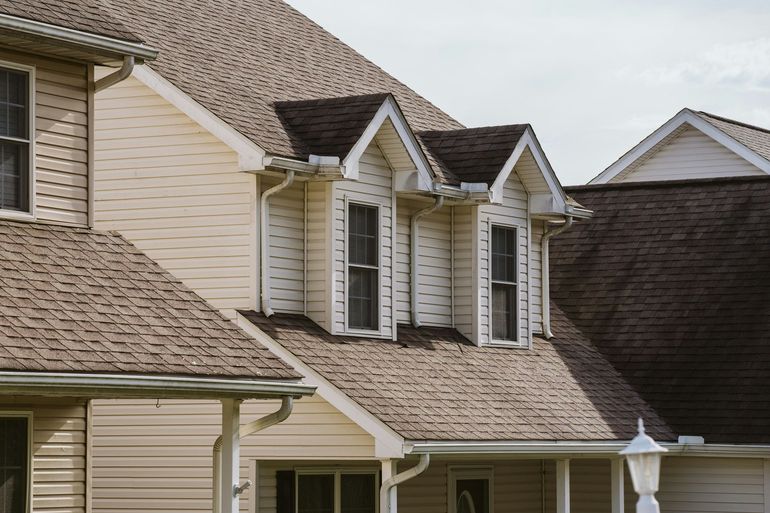 Exterior of a beige suburban house with multiple dormer windows and a shingled roof