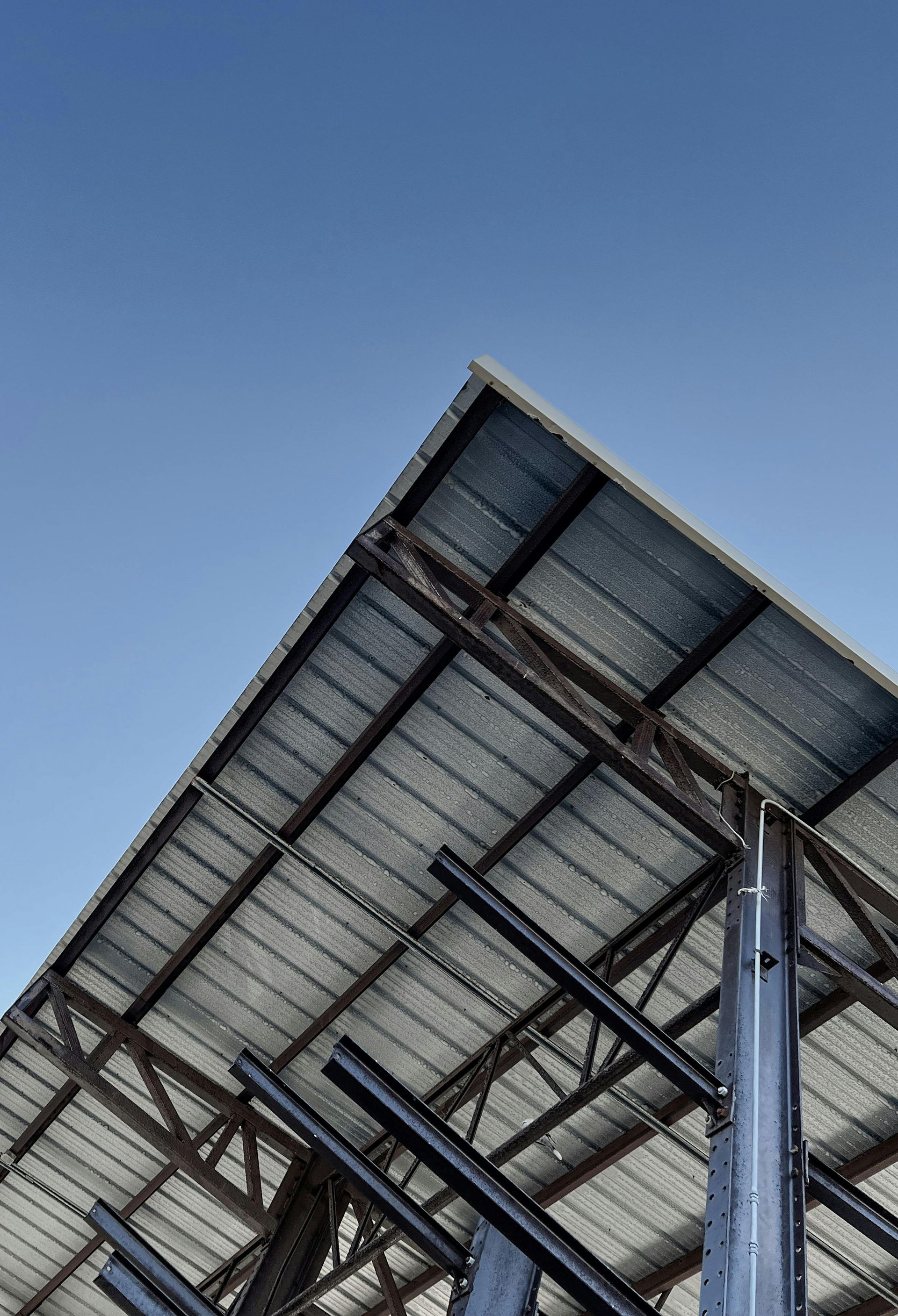 Metal roof structure viewed from below against a clear blue sky