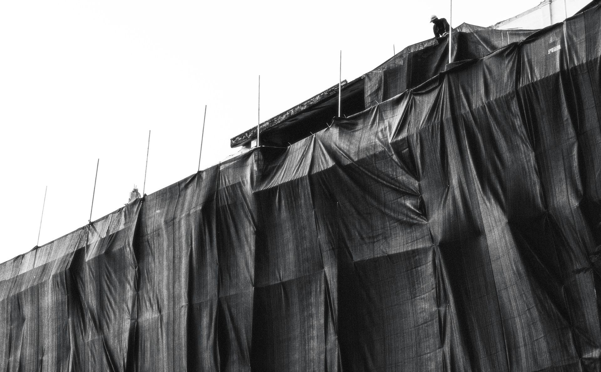 Black tarp-covered scaffolding along a building facade with vertical poles against a bright sky