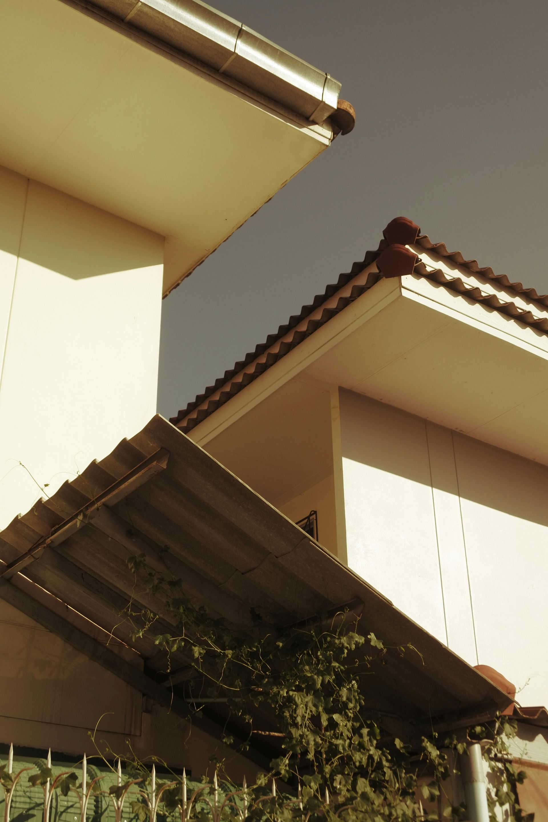 Sunlit view of beige houses with brown tiled roofs and eaves, seen from below