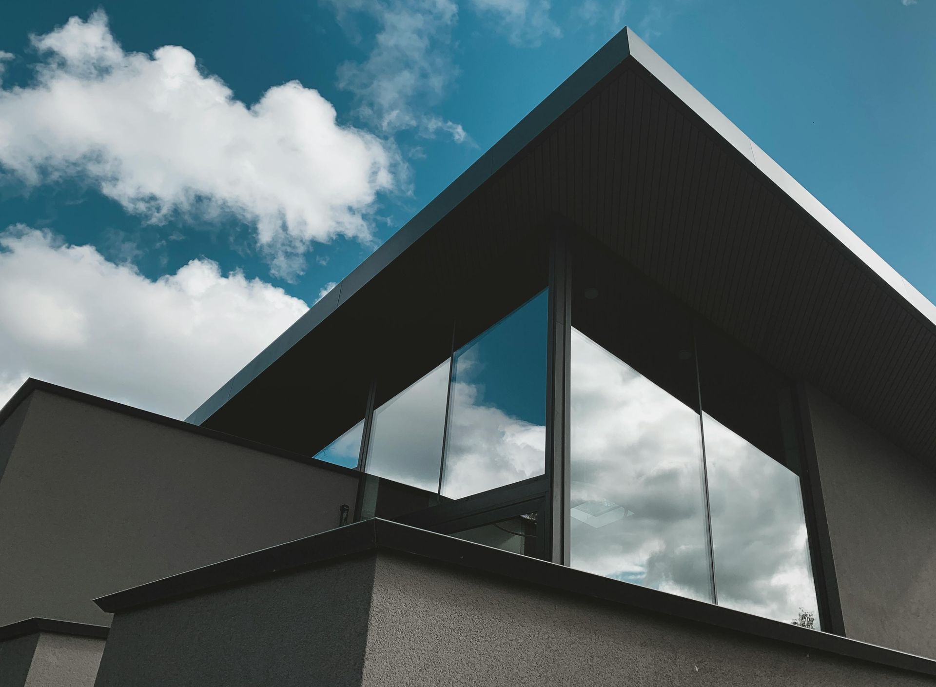 Modern building with dark angular roof and reflective glass under a cloudy blue sky