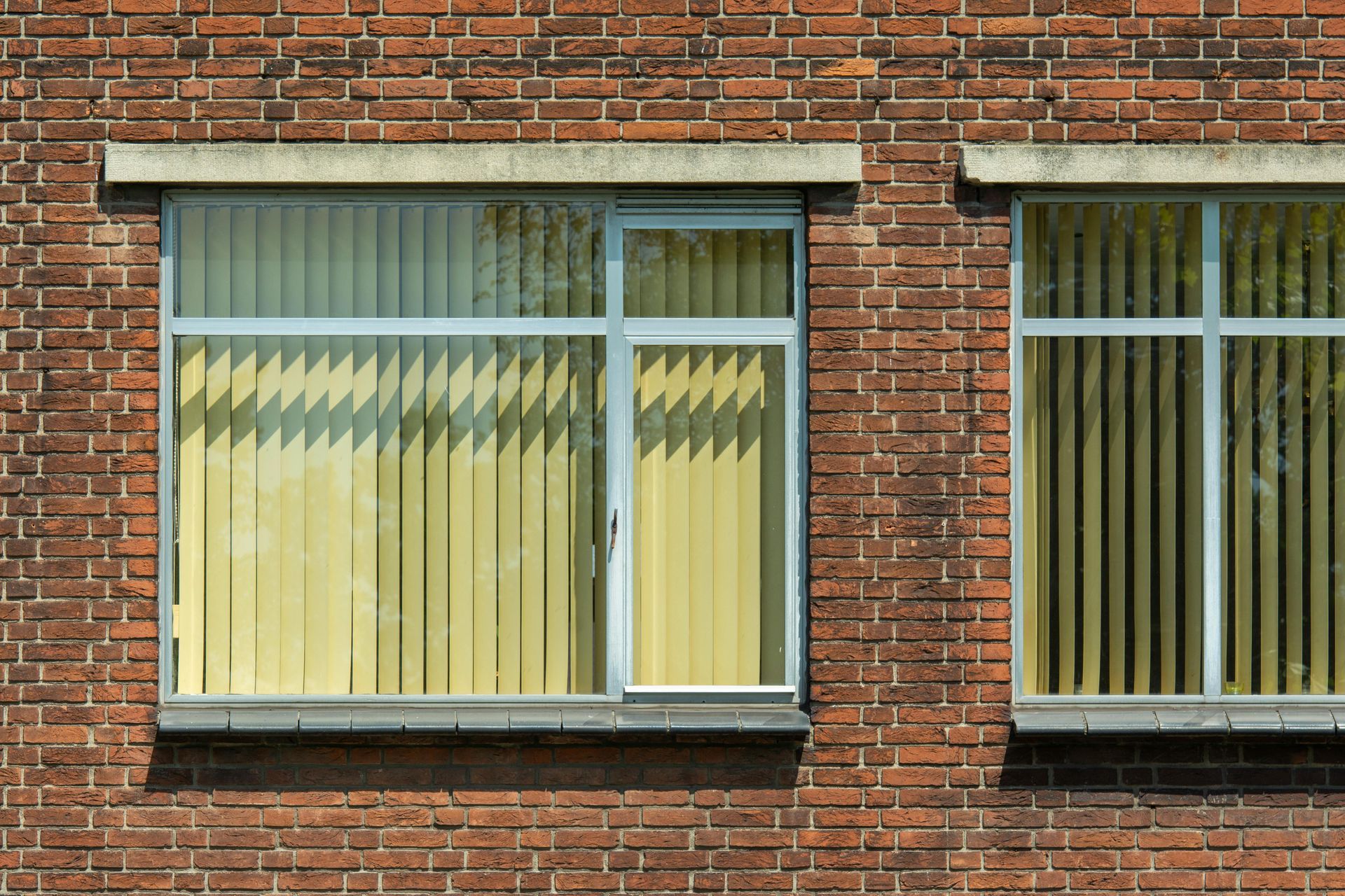 Brick apartment building windows with beige vertical blinds and a zigzag curtain pattern inside