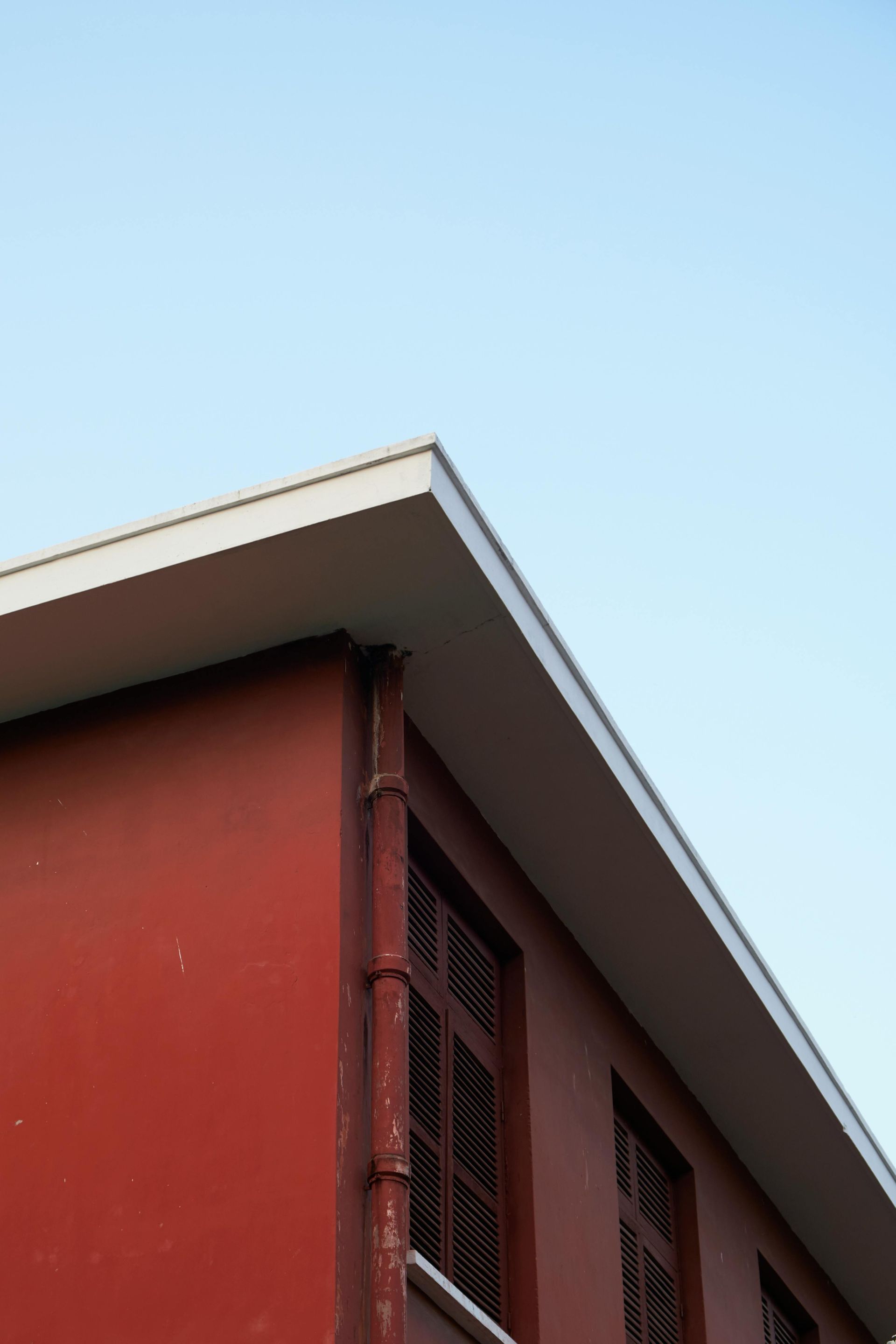 Red building corner with white roof trim against a clear blue sky