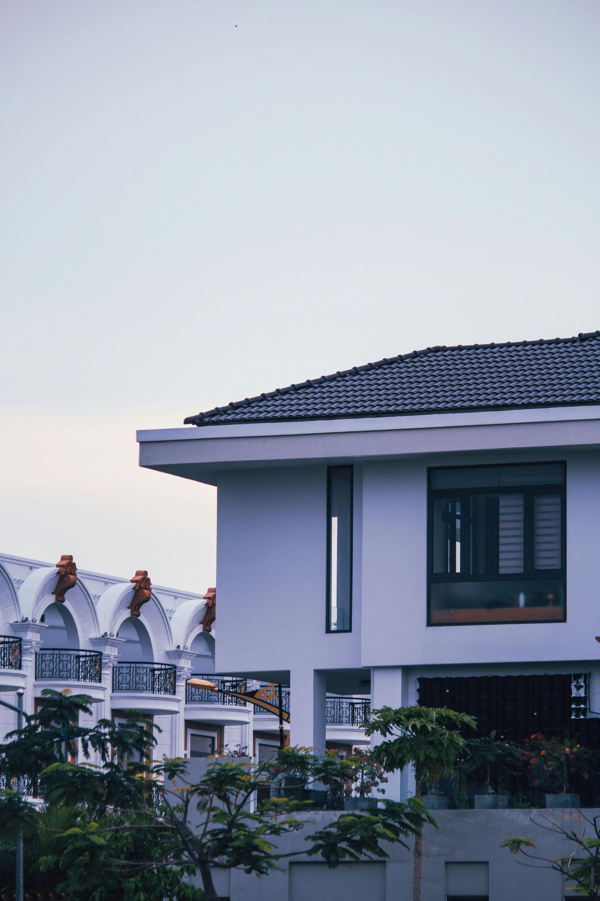 Modern house with a dark tiled roof beside white buildings under a pale sky
