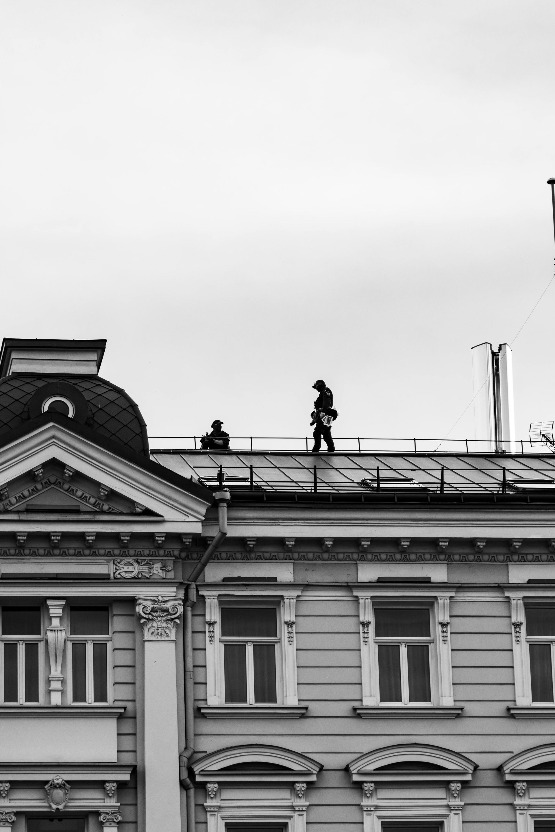 Two workers on a rooftop above a historic building under a cloudy sky