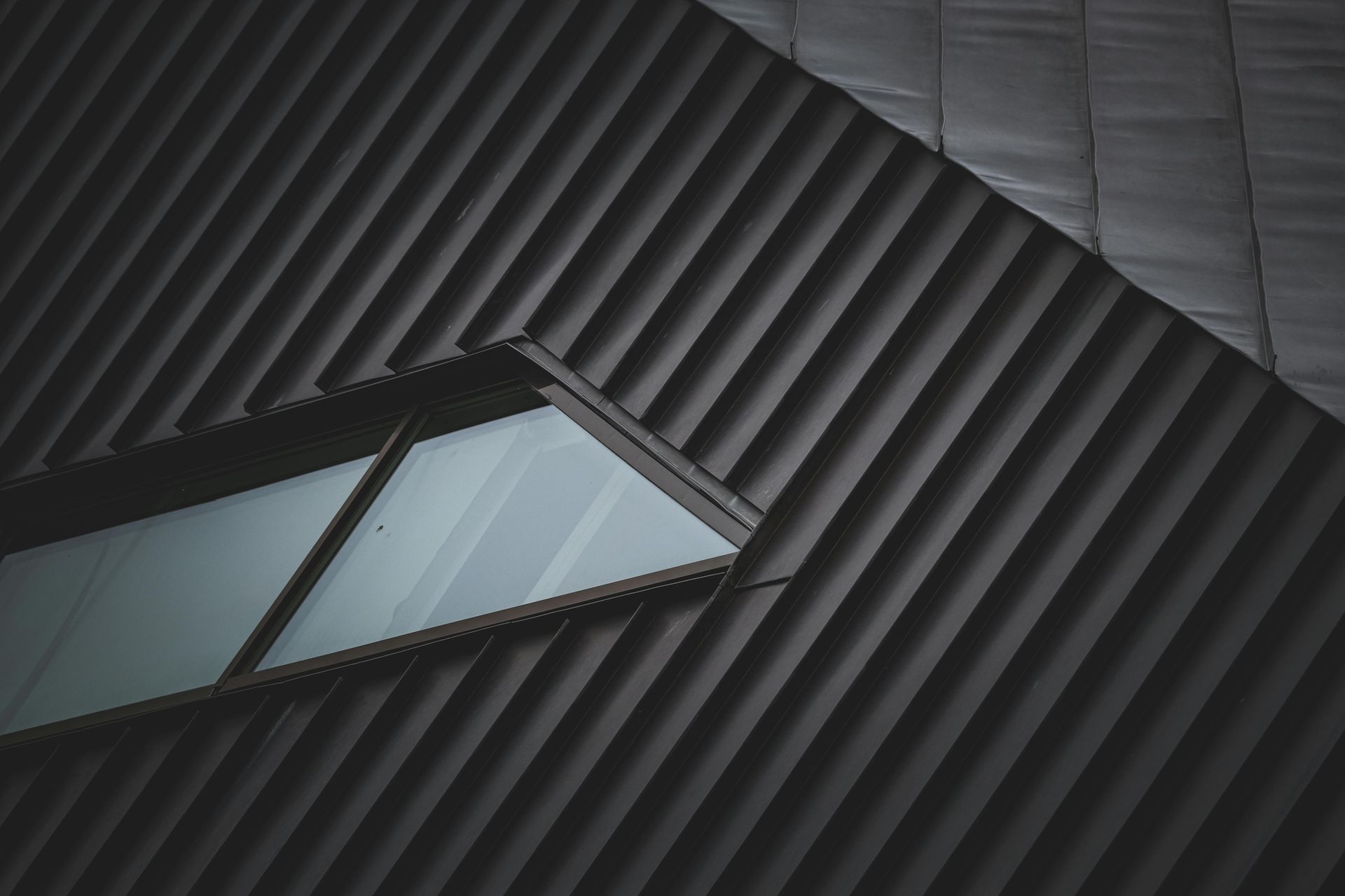 Abstract close-up of dark ribbed metal panels with a diagonal skylight window