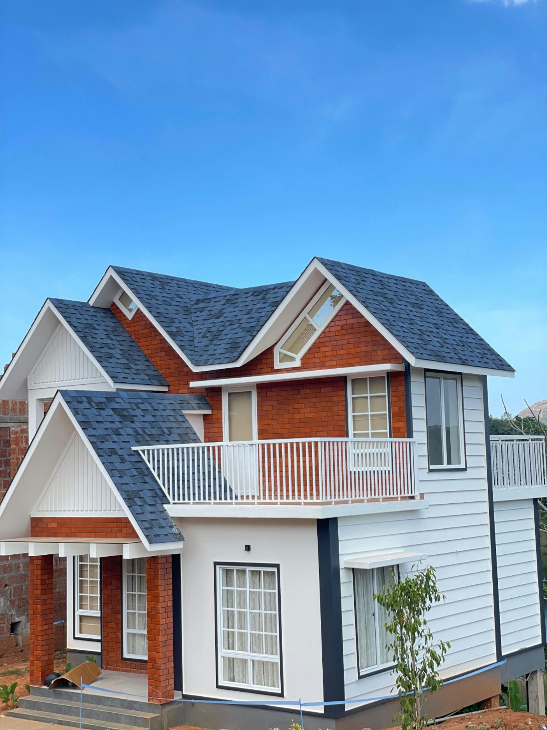 Two-story house with white siding, red brick accents, and a blue roof under a clear sky