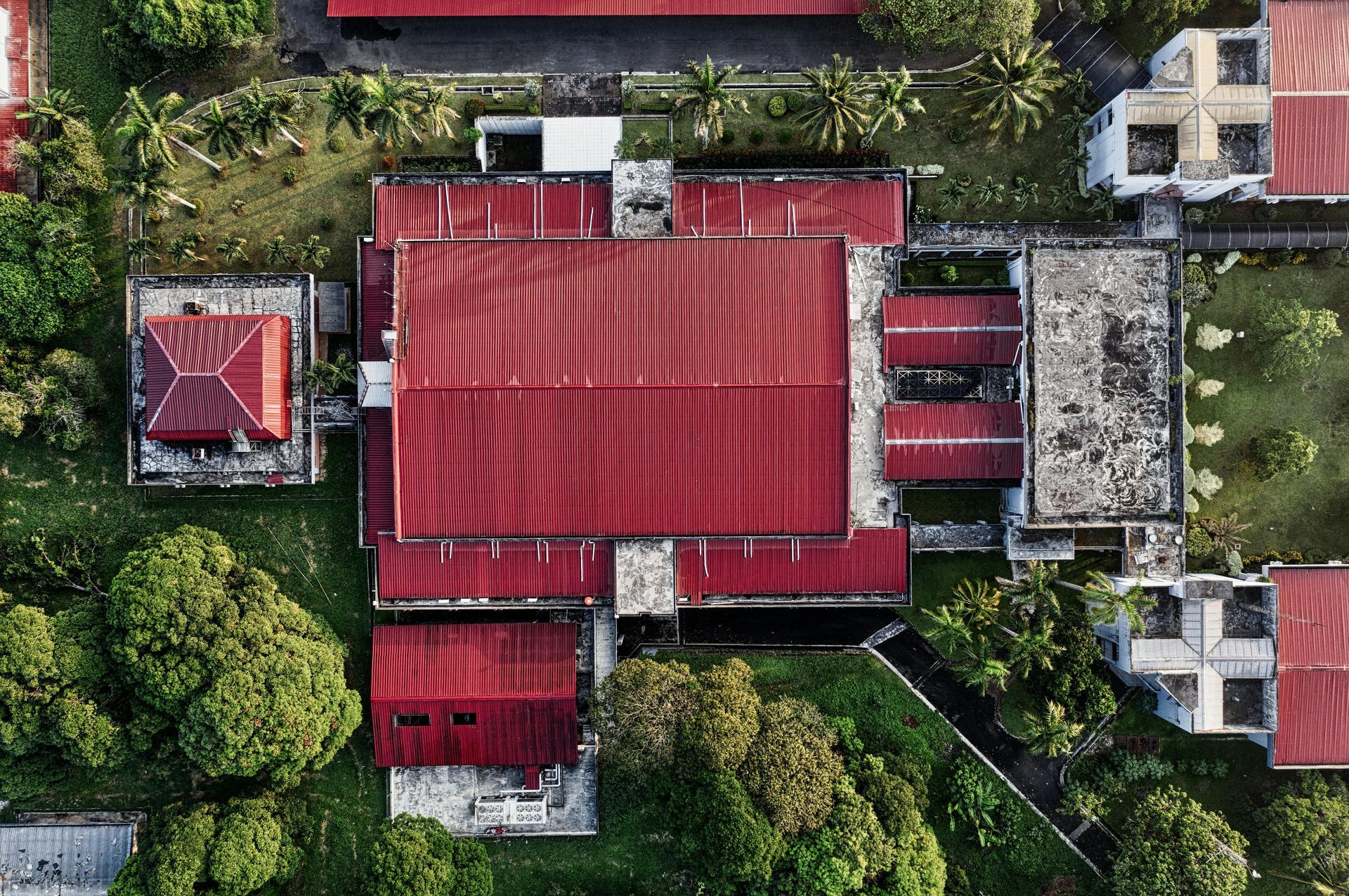 Aerial view of a red-roofed house surrounded by green trees and neighboring buildings.