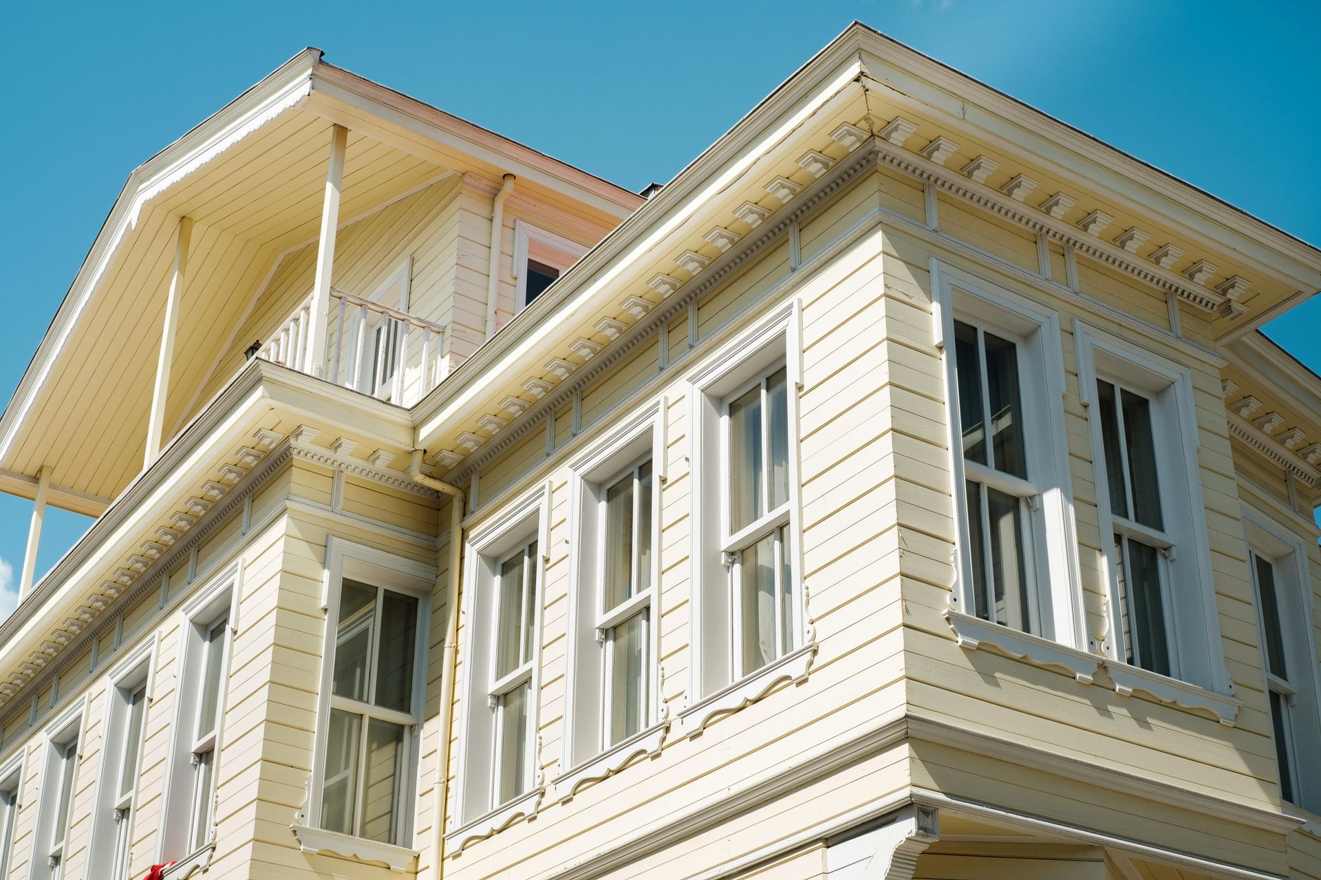 White Victorian-style house exterior with ornate trim, tall windows, and a sunny blue sky